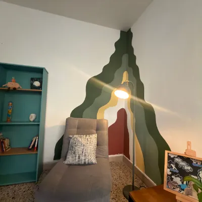 Consultorio con un diván gris, una lámpara y un mural de montañas en tonos verdes y ocres