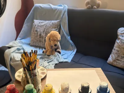 Sala de terapia con sofá azul, un peluche y pinturas sobre la mesa